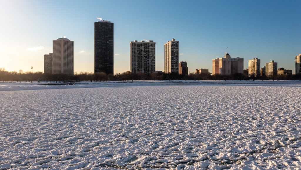 Vista dello skyline del quartiere Edgewater grattacieli residenziali dall'acqua ghiacciata del lago Michigan vicino alla spiaggia di Foster con il lungolago coperto di neve.