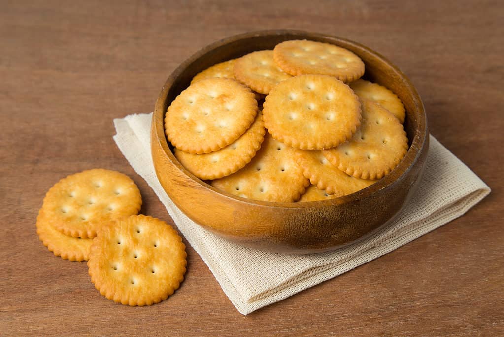 Biscotti cracker salati rotondi in ciotola di legno che mettono su lino e sfondo di legno.