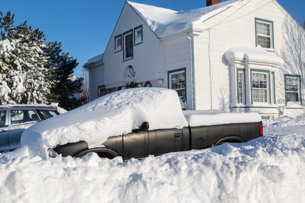 Mucchi di neve seppelliscono un camion e una casa in un sobborgo nordamericano.