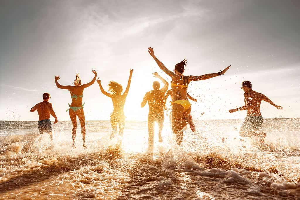 Un grande gruppo di amici corre e salta sulla spiaggia del mare al tramonto.