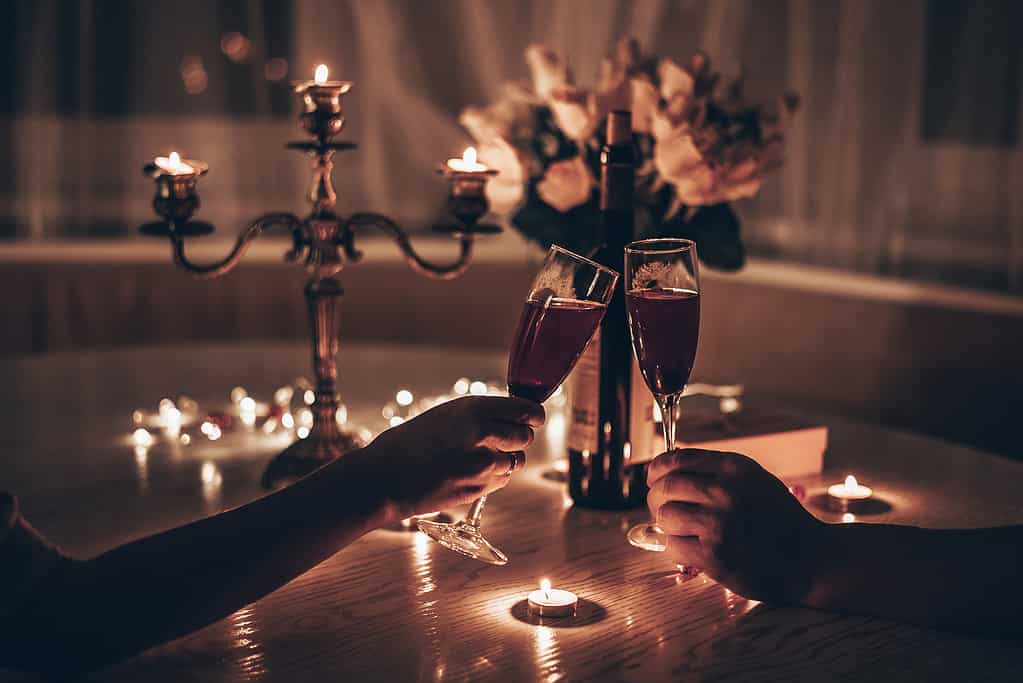 Mani uomo e donna che tengono bicchieri di vino con una romantica cena a lume di candela a tavola a casa.  Mani uomo e donna che tengono un bicchiere di vino.  Concetto di San Valentino o data a lume di candela di notte.
