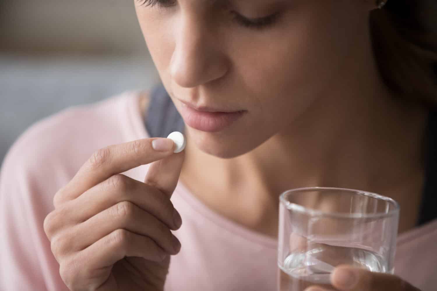 Primo piano immagine ritagliata ragazza di razza mista millenaria con pillola e bicchiere di acqua fresca, prendendo medicine dal mal di testa, mal di stomaco o prendendo vitamine, farmaci sedativi, concetto di assistenza sanitaria