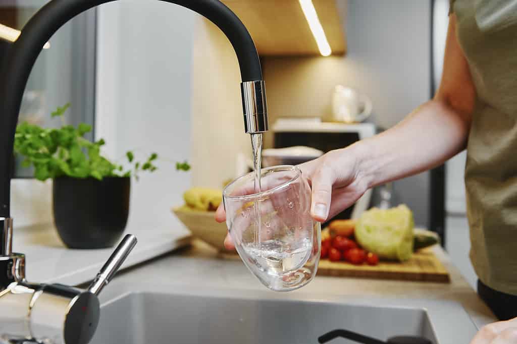 Donna che versa acqua dal rubinetto nel bicchiere in cucina