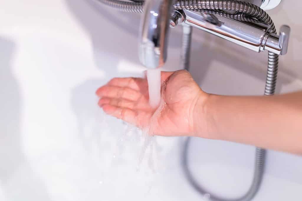 Bella donna che tocca la superficie dell'acqua nella vasca da bagno per controllare la temperatura dell'acqua prima di entrare nella vasca.  Concetto di benessere e idroterapia.