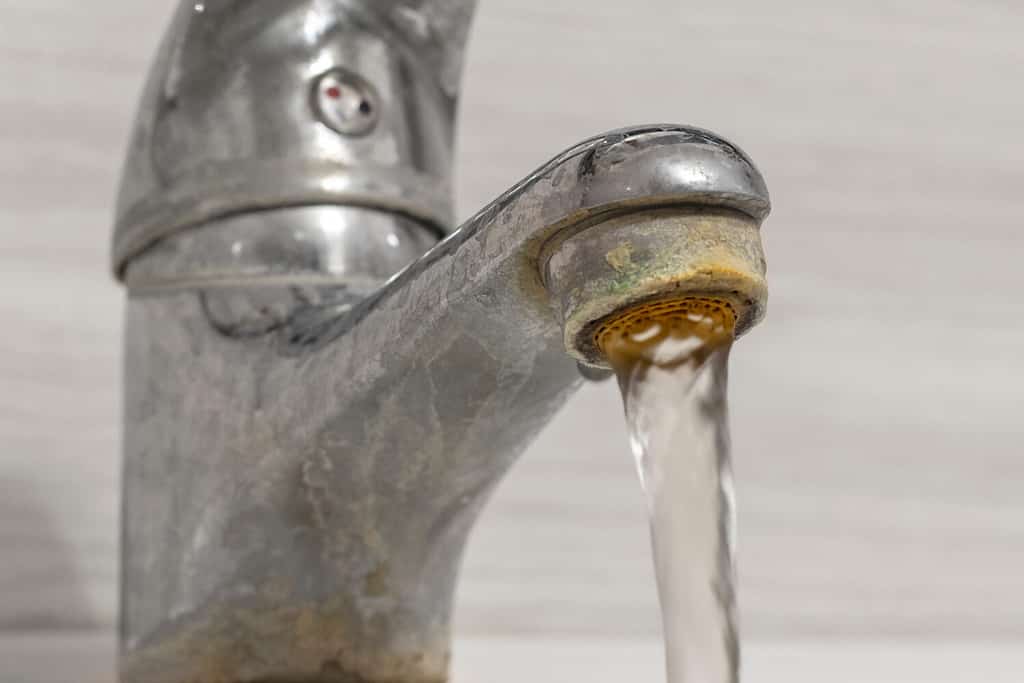 Vecchio rubinetto del lavandino del bagno contaminato da calcio e sporcizia.  L'acqua dura scorre da un vecchio aeratore del rubinetto.