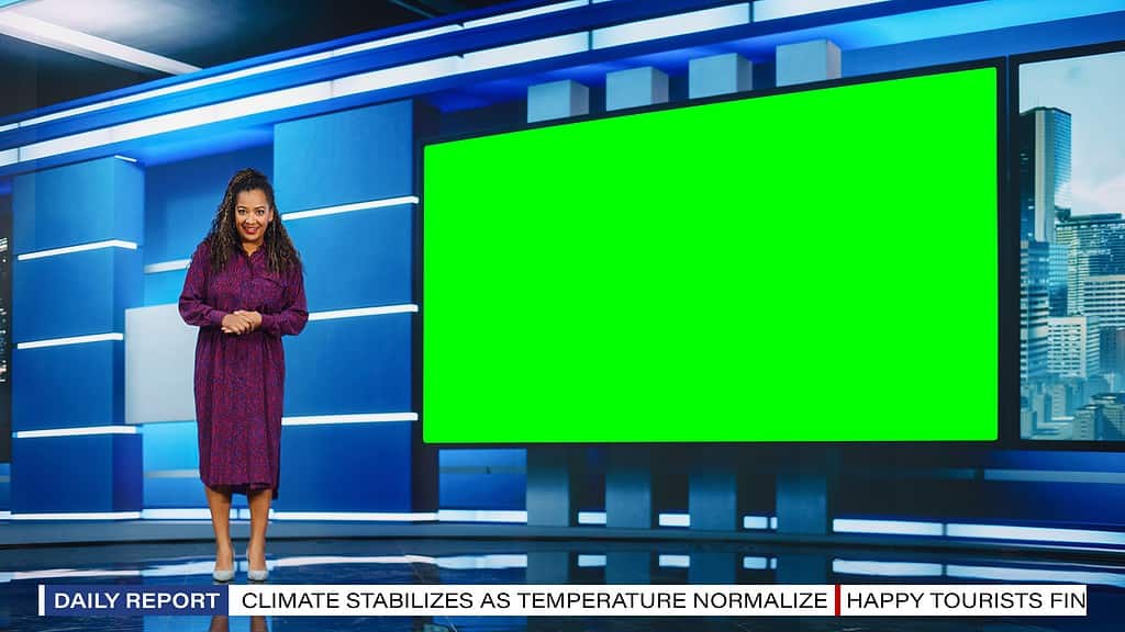 Presentatrice donna dalla pelle marrone in piedi nello studio della redazione, utilizza il grande schermo Chroma Key verde.  News Achor, presentatore parla del tempo.  La donna è nel frame di sinistra.  Uno "schermo verde" vuoto è alla sua destra.