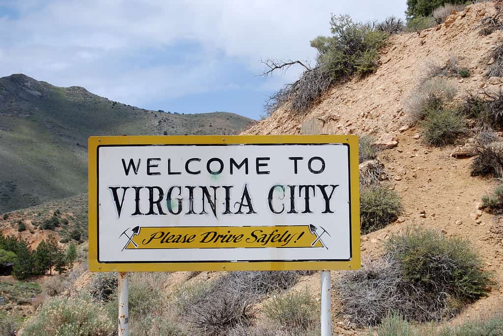Segno della città della Virginia.  Cartello bianco con pesce rosso/cartellone giallo che dice: Benvenuti a Virginia City, Nevada.  Si prega di guidare in sicurezza/ 