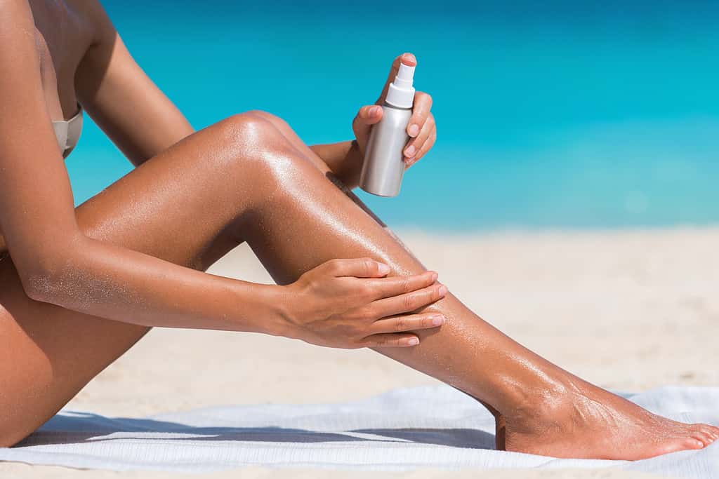 Donna che spruzza crema solare sulla gamba: il miglior indice UV per abbronzarsi