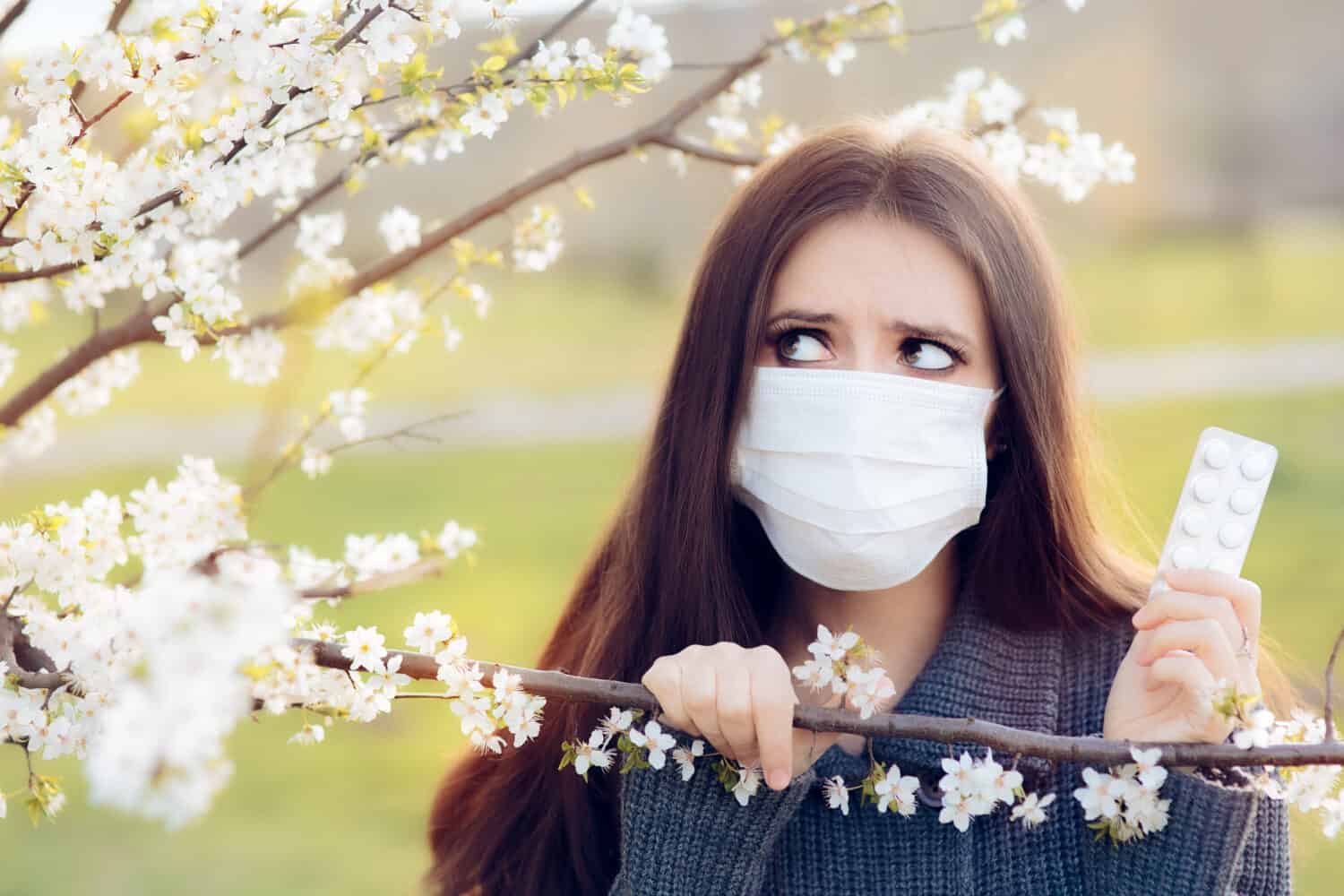 Donna con maschera respiratoria che combatte le allergie primaverili all'aperto - Ritratto di una donna allergica circondata da fiori stagionali che indossa una maschera protettiva