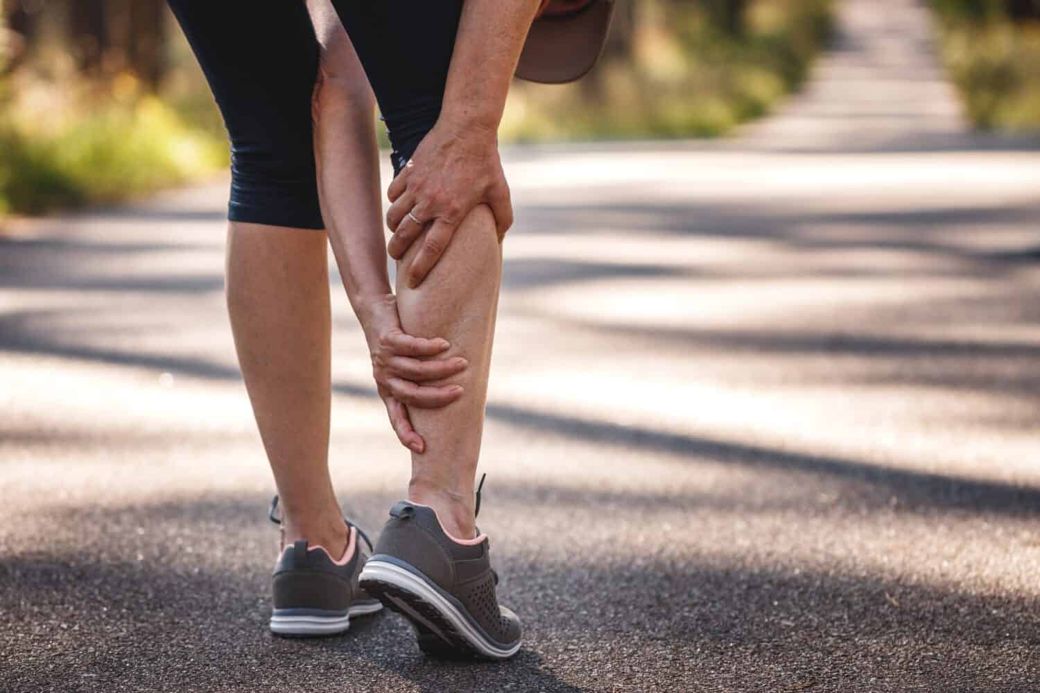 Donna che sente dolore alle gambe durante il jogging.  Crampi muscolari al polpaccio.  Sottovalutare l'esercizio di riscaldamento prima di correre