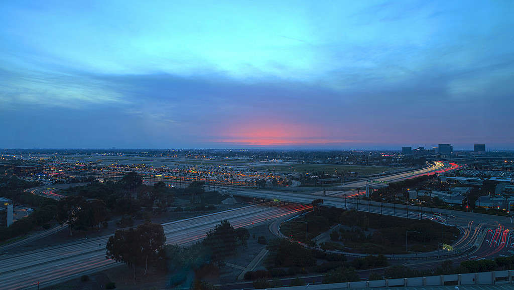 Vista aerea dell'aeroporto John Wayne di Orange County, California, al tramonto con la pioggia nei sentieri leggeri dell'aria attraverso l'autostrada 405 di fronte.