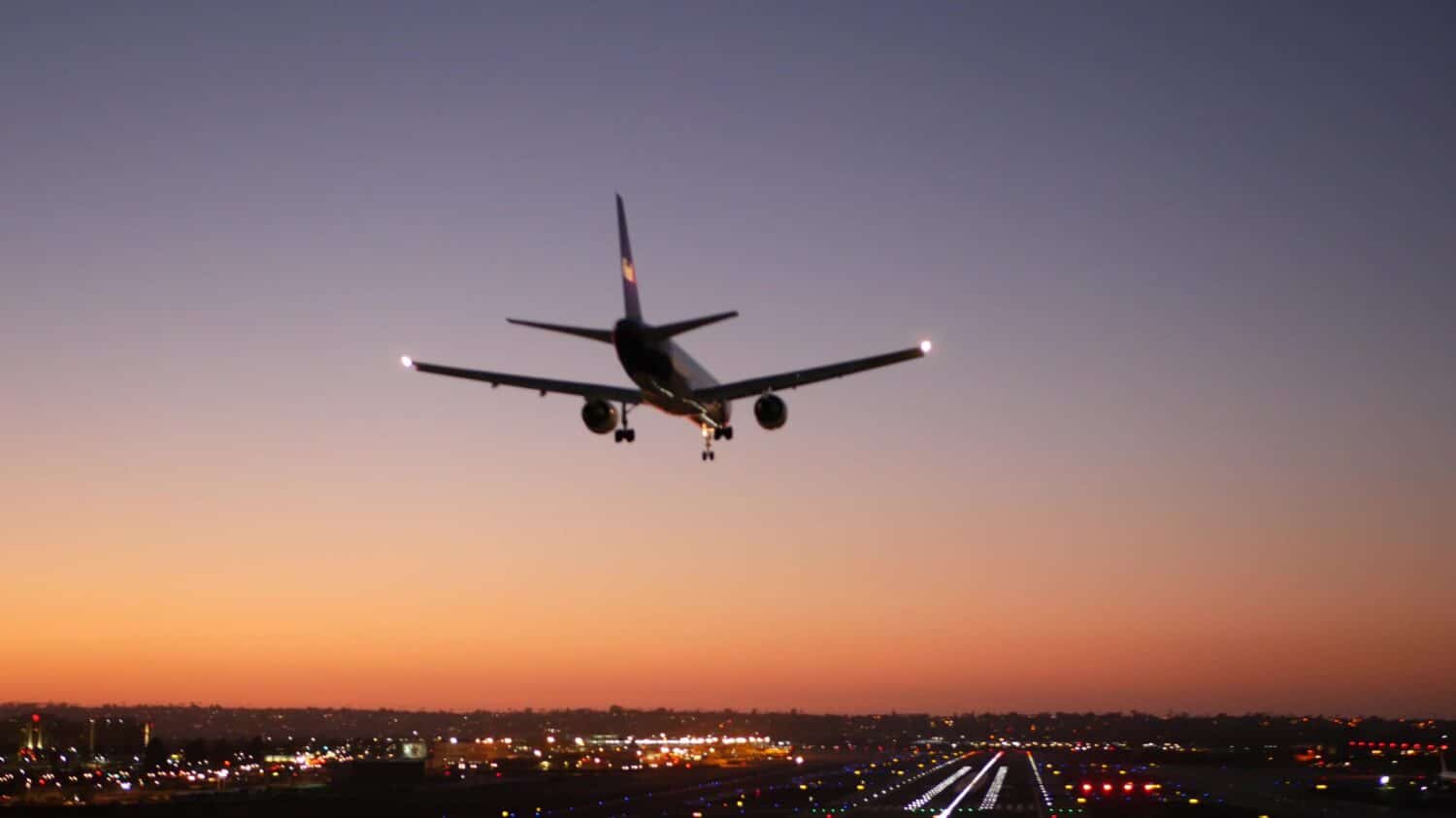 Luci della pista dell'aeroporto di notte, aereo o aereo che atterra sulla pista di atterraggio, crepuscolo e tramonto.  Jet aereo di linea che arriva all'aerodromo, campo d'aviazione di San Diego, California USA.  Aerei che volano a mezz'aria nel cielo.