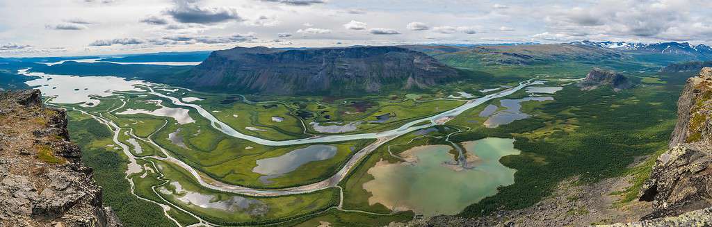 Vista panoramica panoramica aerea dalla cima della roccia di Skierffe sulla valle glaciale del delta del fiume Rapadalen nel parco nazionale di Sarek con meandri, laghi, montagne, betulle.