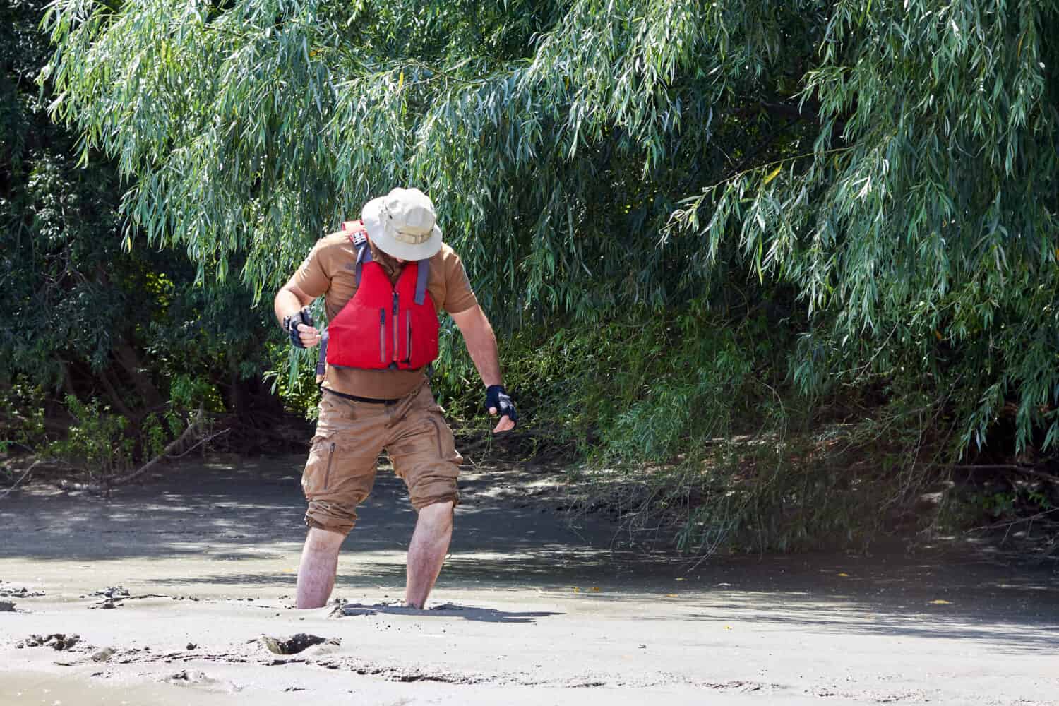 Uomo in piedi nel fiume di sabbie mobili naturali, sedimenti di argilla, affondamento, annegamento di sabbia veloce, bloccato nel terreno