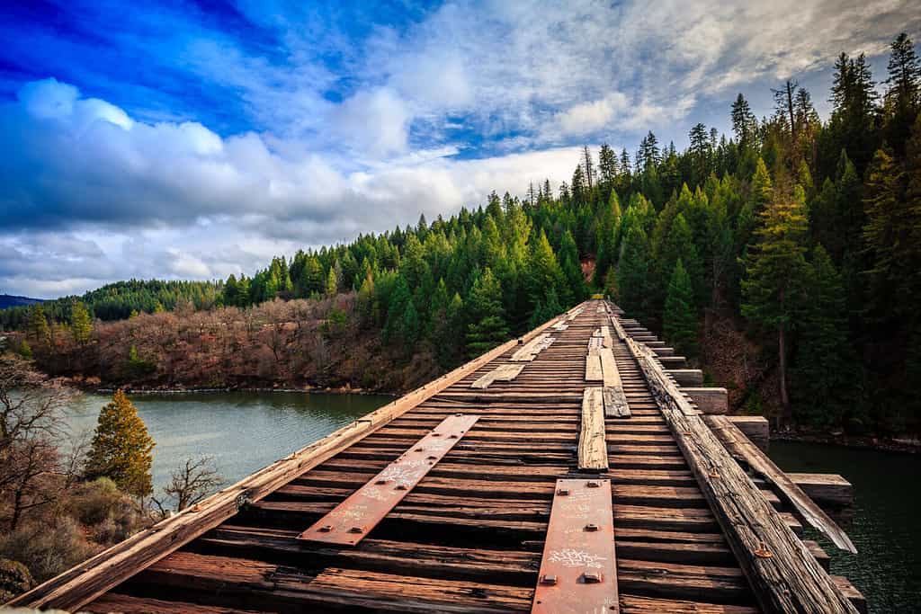 Un ponte di legno si inarca su un lago, circondato da alberi. 