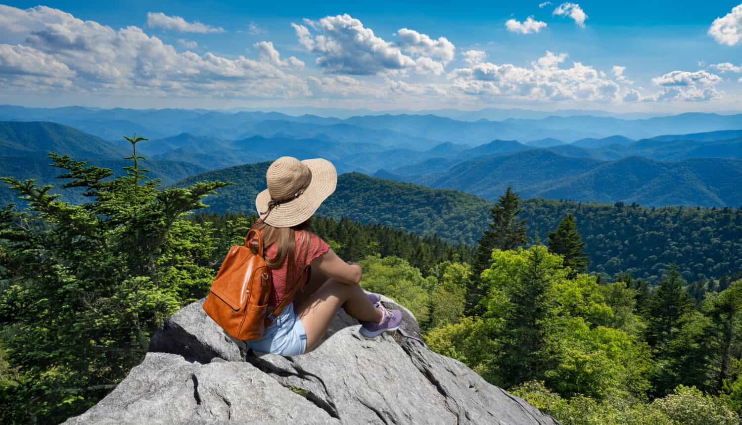 Ragazza della viandante che si siede su un bordo della scogliera che gode della vista panoramica di estate.  Donna che si rilassa in cima alla montagna autunnale, sopra le nuvole.  Blue Ridge Parkway ,vicino a Asheville, North Carolina, Stati Uniti d'America.