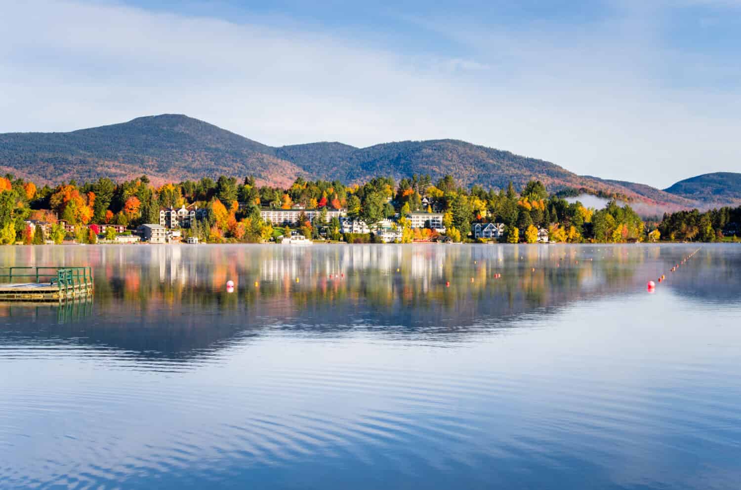 Vista del villaggio di montagna di Lake Placid da un lago specchio nebbioso all'alba