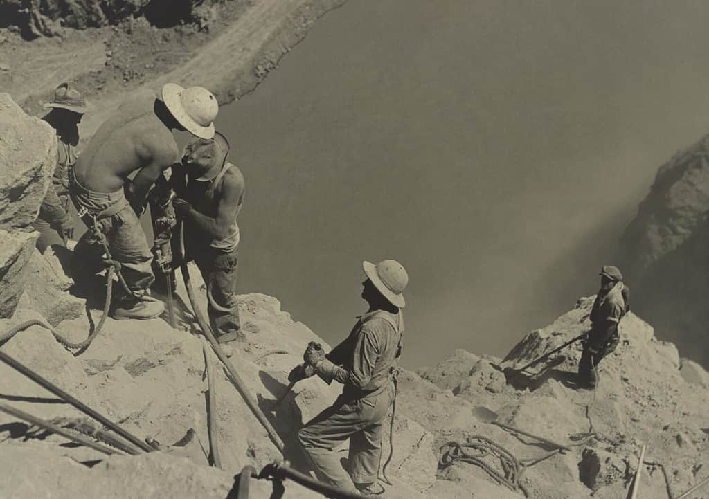 Lavoratori nel sito della diga di Boulder nel 1934. Sono scalatori alti che perforano le pareti del canyon sopra il fiume Colorado.