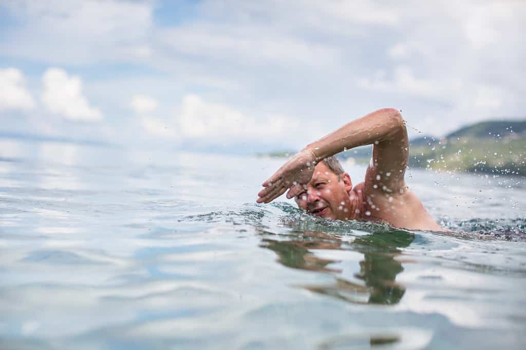 Uomo anziano che nuota nel mare/oceano - godendosi la pensione attiva, divertendosi, prendendosi cura di se stesso, rimanendo in forma