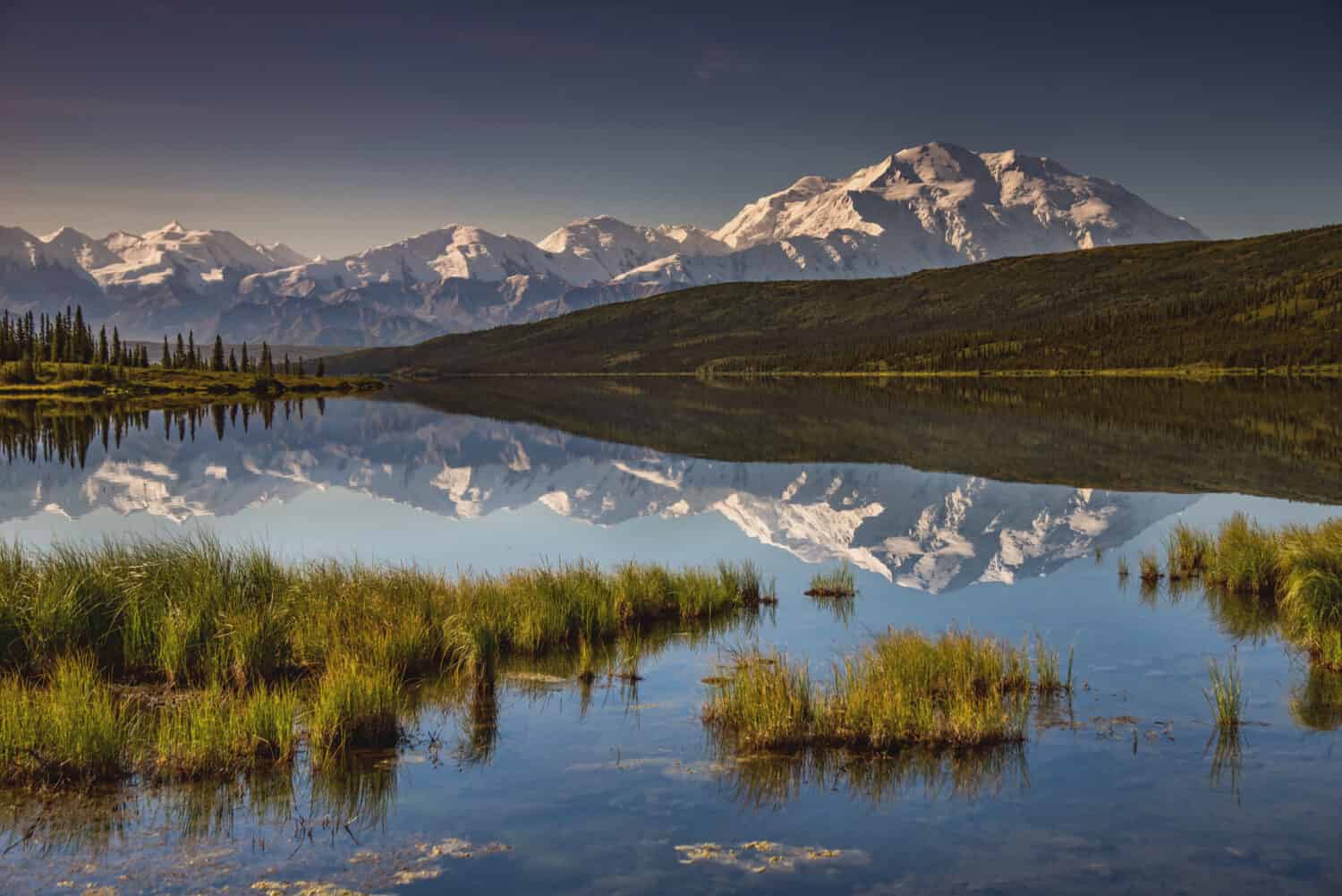 vista del monte denali dell'Alaska riflessa nel calmo Wonder Lake, con sopra un cielo blu chiaro