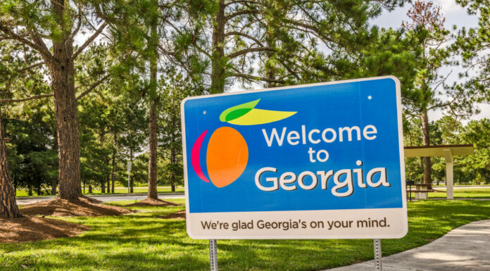 Un cartello di benvenuto in Georgia davanti a un prato ondulato con alberi sullo sfondo.