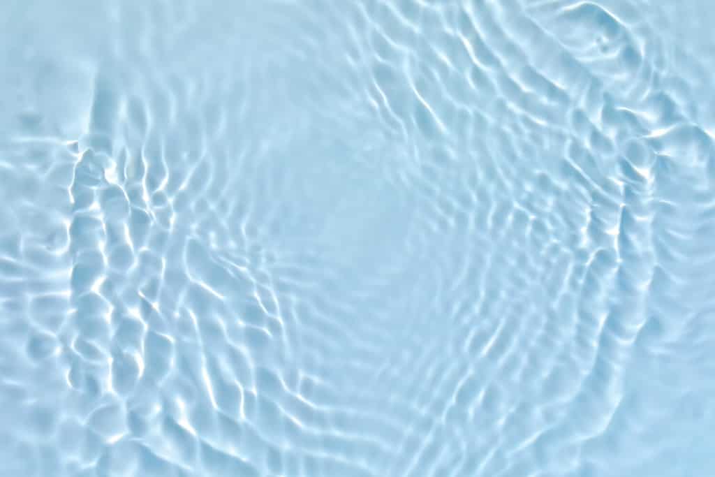 Struttura della superficie dell'acqua calma e trasparente di colore blu trasparente sfocato con spruzzi e bolle.  Sfondo astratto alla moda.  Onde d'acqua alla luce del sole.