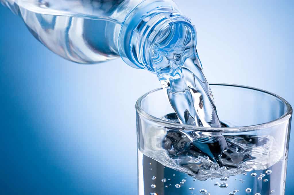 Versare l'acqua dalla bottiglia nel bicchiere su sfondo blu