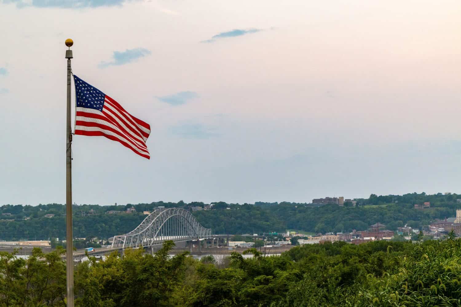 Una vista della bandiera americana e Julien Dubuque Bridge contro il cielo blu al tramonto nella città di Dubuque, Iowa, Stati Uniti
