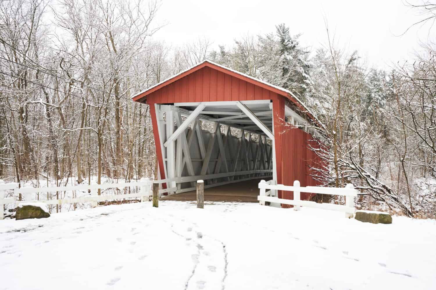 La strada di everett ha coperto il ponte nel parco nazionale della valle di Cuyahoga.  Il ponte è rosso con interni bianchi.  È una giornata nevosa e gli alberi vicini nella foresta sono ricoperti di soffice bianco.