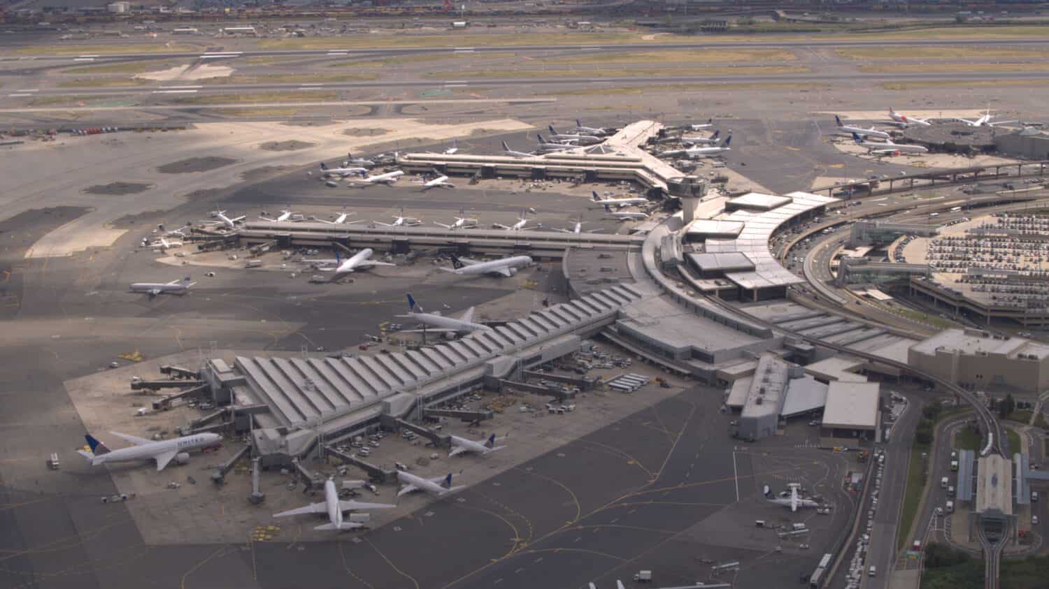 ANTENNA, PRIMO PIANO: Volare sopra gli aeroplani parcheggiati sul piazzale in attesa che i passeggeri salgano a bordo della jetway e inizino il loro viaggio di viaggio.  Terminal dell'aeroporto internazionale di New York Newark