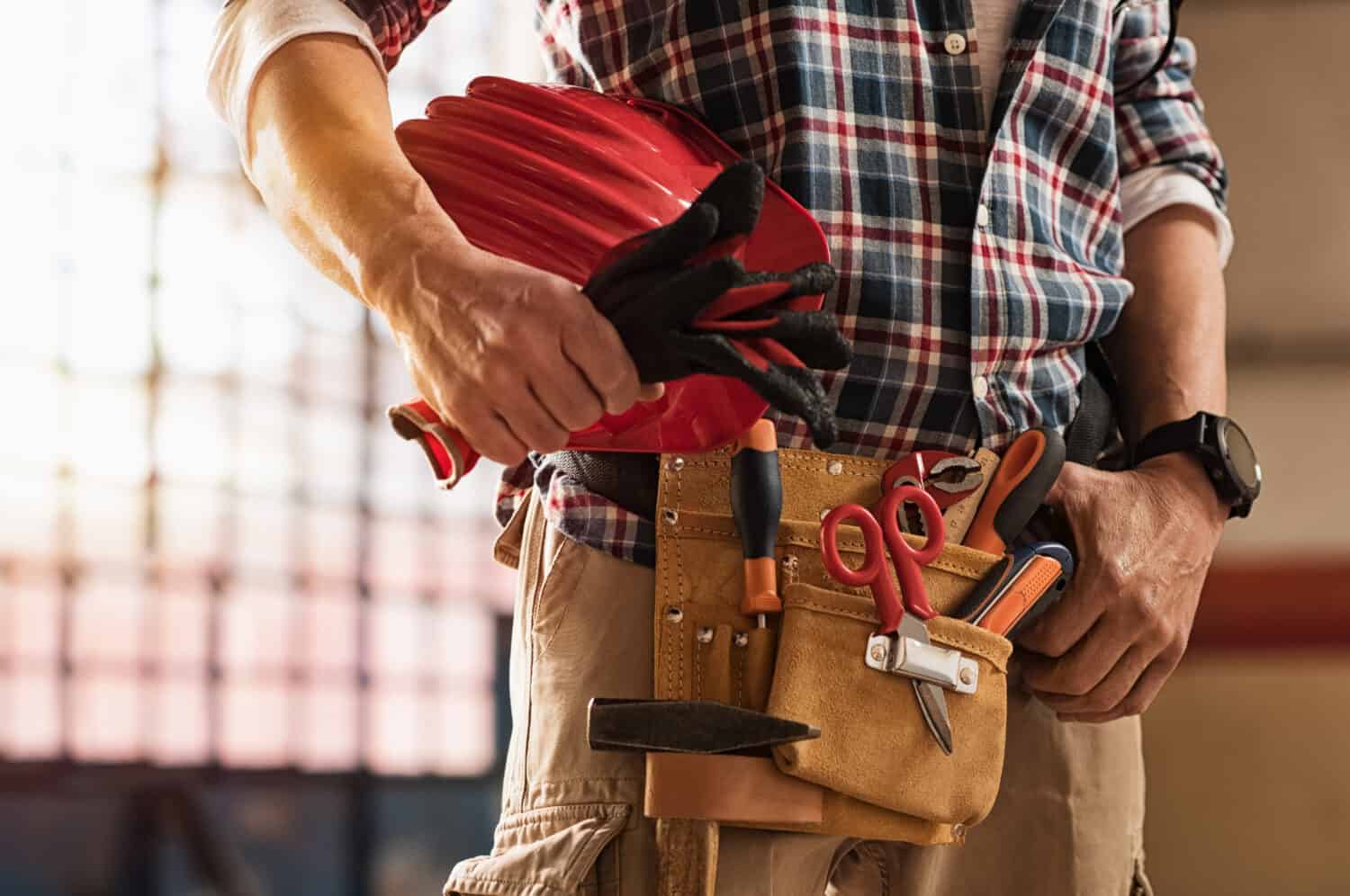 Primo piano delle mani del muratore che tengono elmetto protettivo e attrezzatura da costruzione.  Dettaglio delle mani dell'uomo muratore che tengono i guanti da lavoro e indossano il kit di attrezzi sulla vita.  Tuttofare con cintura porta attrezzi e attrezzatura artigianale.