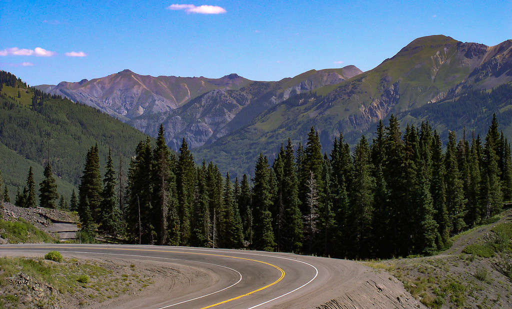 Vista di una cura pavimentata nella Million Dollar Highway in Colorado con alberi e strati di montagne sullo sfondo.