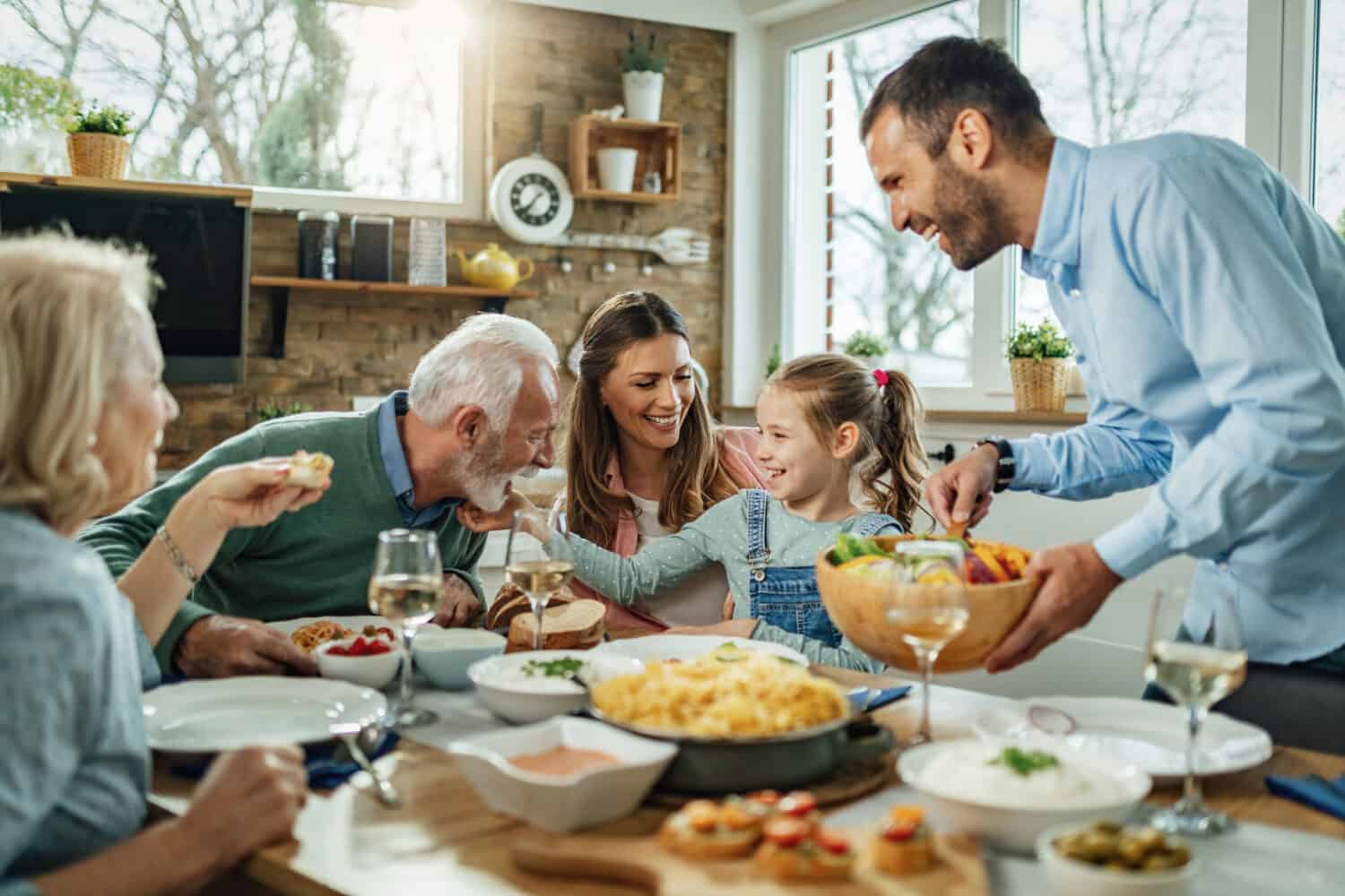 Felice famiglia di più generazioni che si riunisce attorno al tavolo da pranzo e si diverte durante un pranzo. 