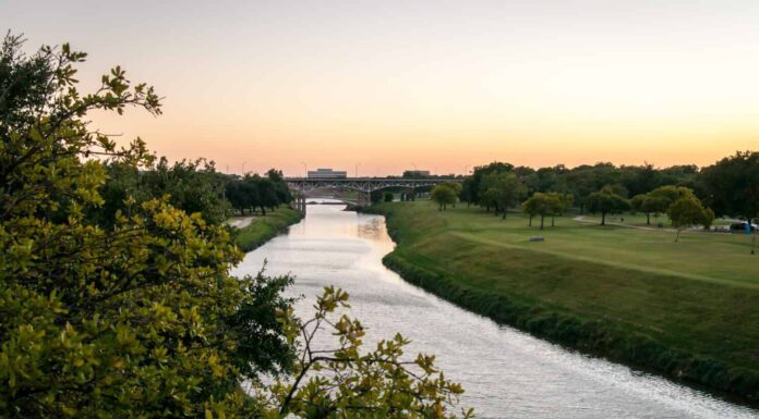 Trinità Fiume Fort Worth, Texas.  Tramonto sull'acqua, colori arancioni e dorati.  Erba verde e alberi in un parco pubblico.  Sera d'estate tranquilla e calma.  Orientamento orizzontale.