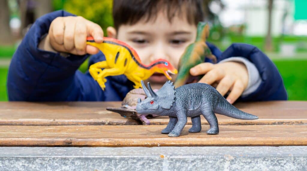 Il ragazzo gioca con i giocattoli dei dinosauri su un tavolo all'esterno