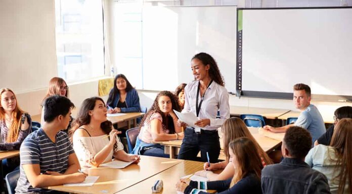 Insegnante di scuola superiore femminile in piedi accanto alla lezione di insegnamento del tavolo degli studenti