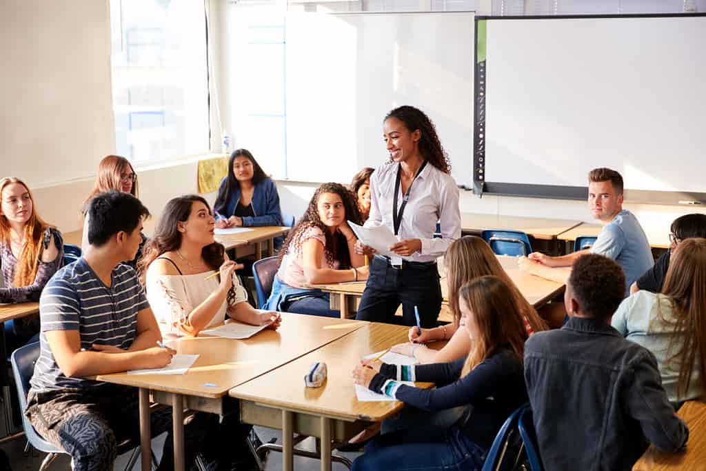 Insegnante di scuola superiore femminile in piedi accanto alla lezione di insegnamento del tavolo degli studenti