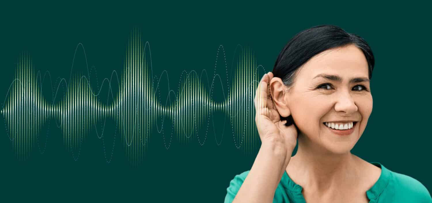 Donna positiva con la mano vicino all'orecchio e con un'onda sonora luminosa su sfondo verde che mostra una varietà di suoni che vanno al suo orecchio.  Concetto di salute uditiva
