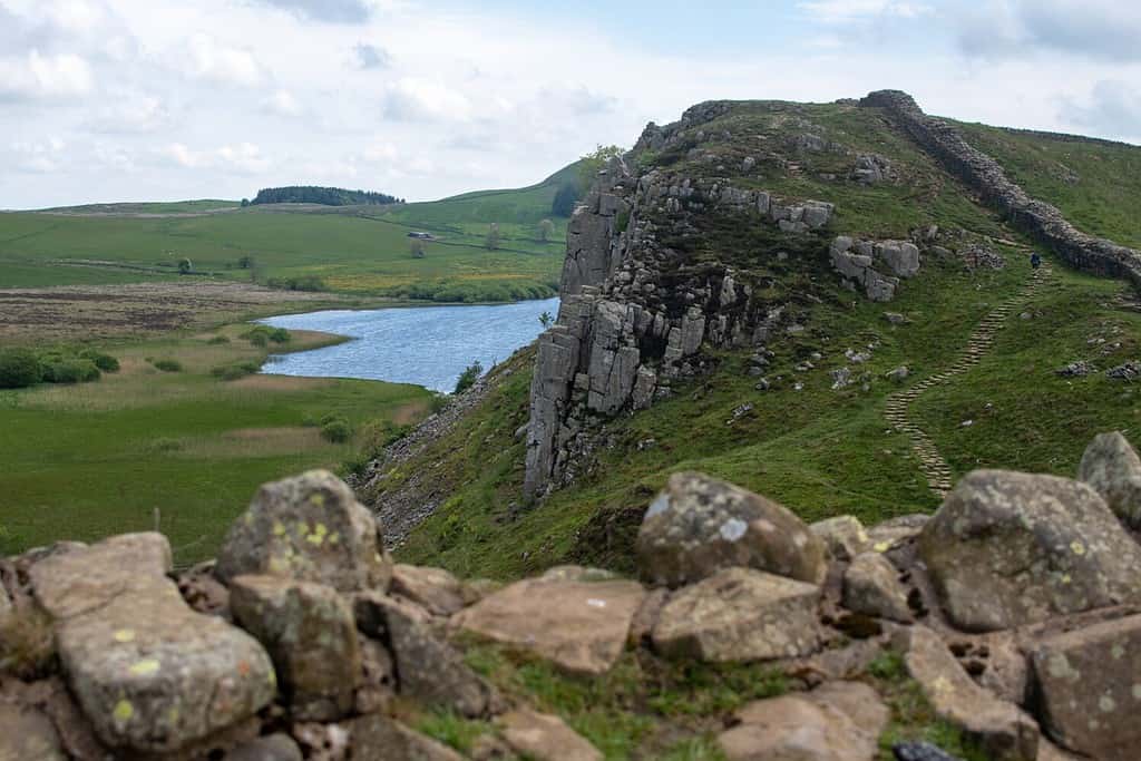 Un tratto del Vallo di Adriano alla base militare romana del milecastle 39, sullo sfondo del lago Whin Sill e Crag Lough in lontananza.  Parco nazionale di Northumberland, Regno Unito
