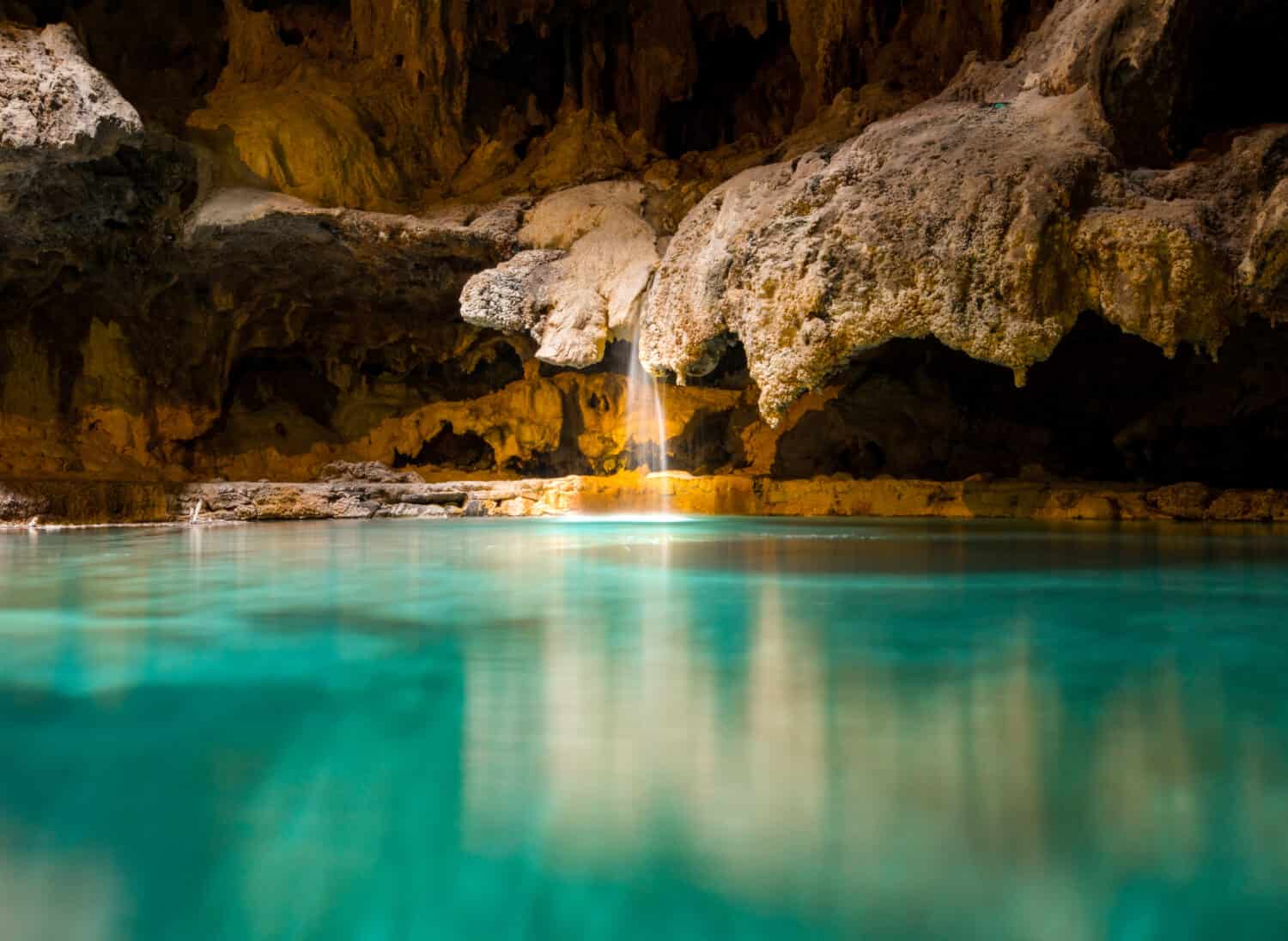 Una piccola cascata pittoresca in una grotta cade in una calda sorgente termale sotterranea blu e verde 