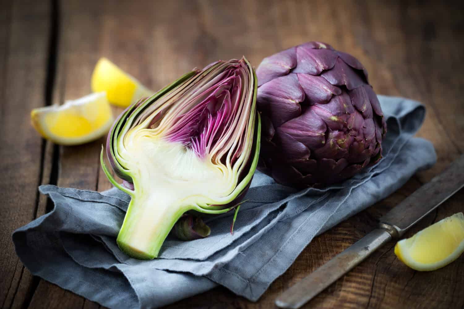 Carciofi viola freschi su fondo di legno rustico scuro con fettine di limone