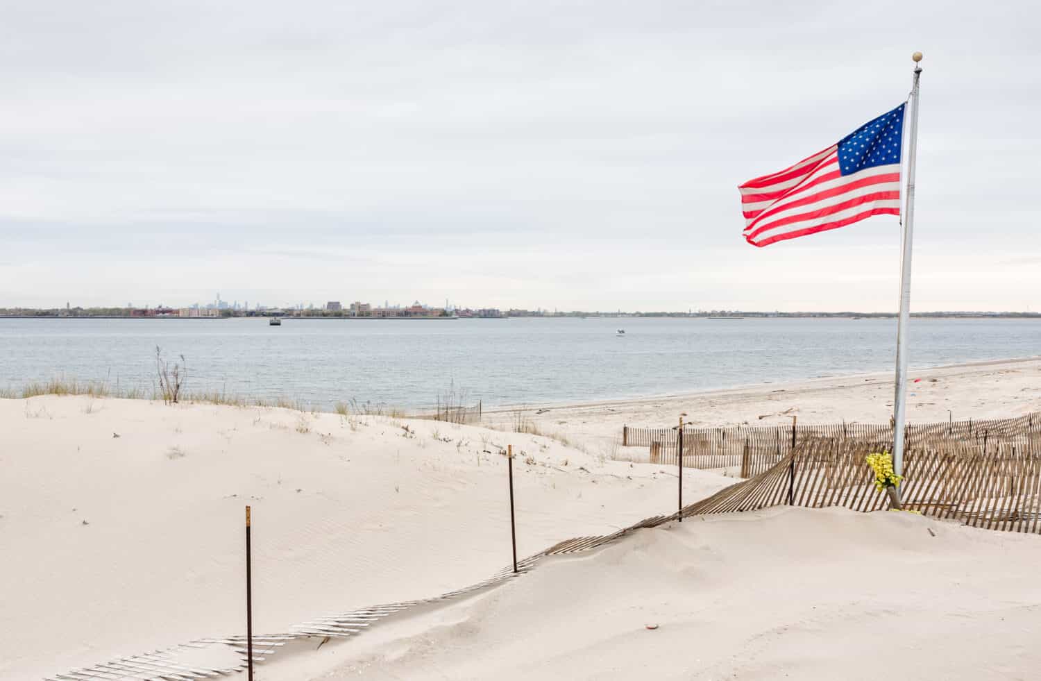 Bandiera americana sulla spiaggia di Breezy Point.  Breezy Point è un quartiere nel quartiere newyorkese del Queens, situato all'estremità occidentale della penisola di Rockaway.  Manhattan sullo sfondo