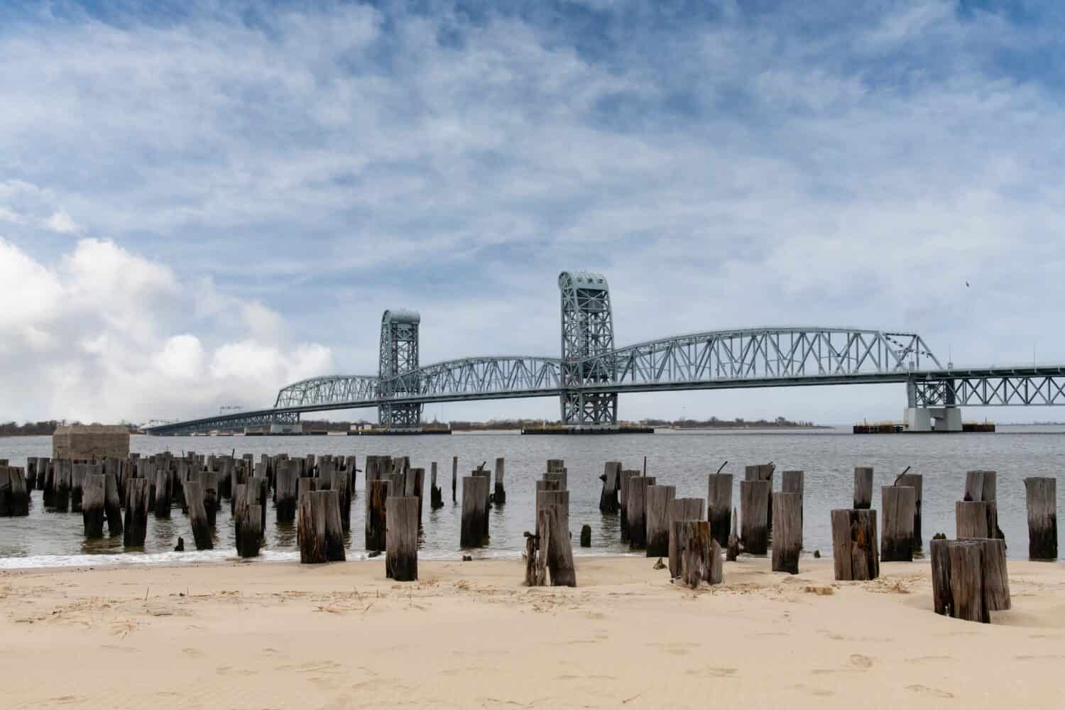 Vista dalla spiaggia di Breezy Point, NY, USA, con resti di pali del molo verso il sollevamento verticale Marine Parkway–Gil Hodges Memorial Bridge (Marine Parkway Bridge crossing Rockaway Inlet 