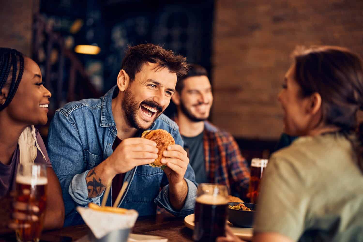 Uomo allegro che mangia hamburger e si diverte mentre si riunisce con gli amici in un bar. 