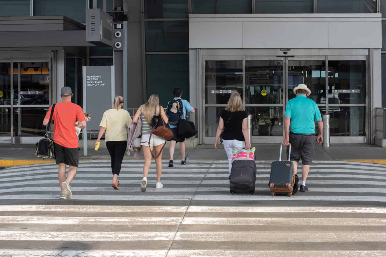 Un gruppo di passeggeri che trasportano bagagli si dirige verso l'ingresso di un terminal aeroportuale. 