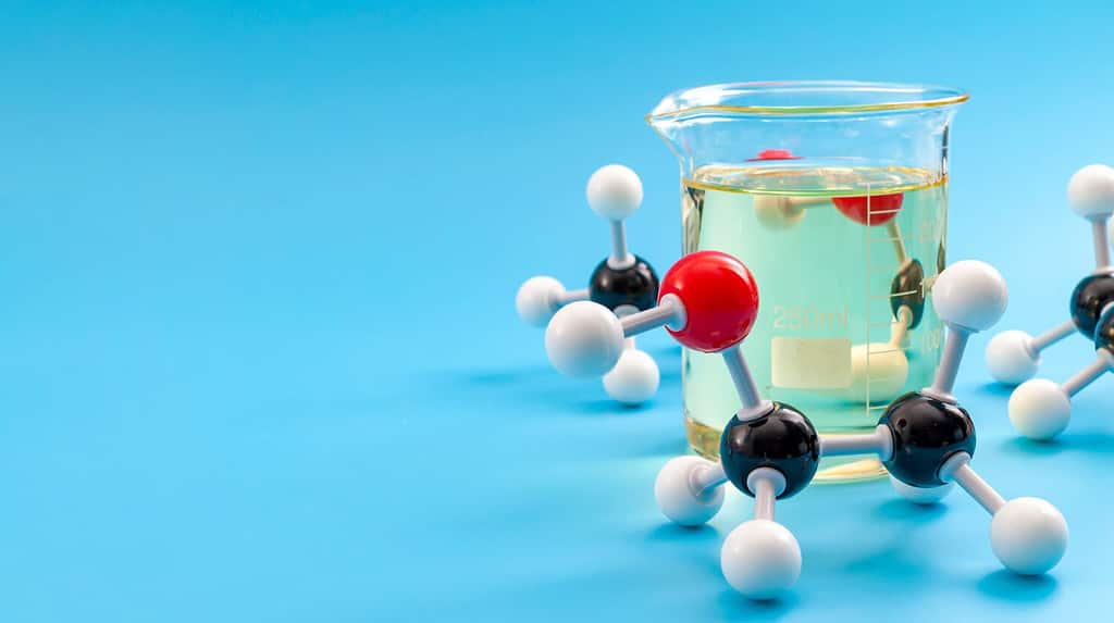 Struttura molecolare dei composti chimici e concetto di chimica organica con modello plastico educativo di molecole di etanolo e pallone di vetro isolato su sfondo blu con spazio di copia