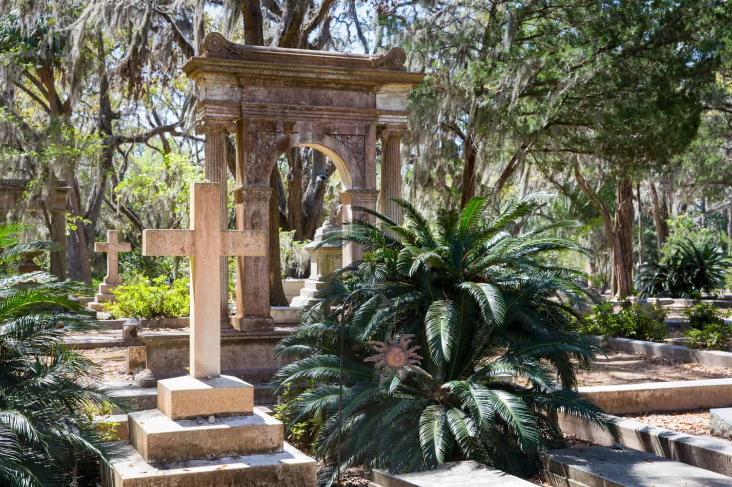 Cimitero storico di Bonaventura a Savannah, GA.  Scena serena con croce prominente in primo piano, vegetazione lussureggiante e muschio spagnolo.