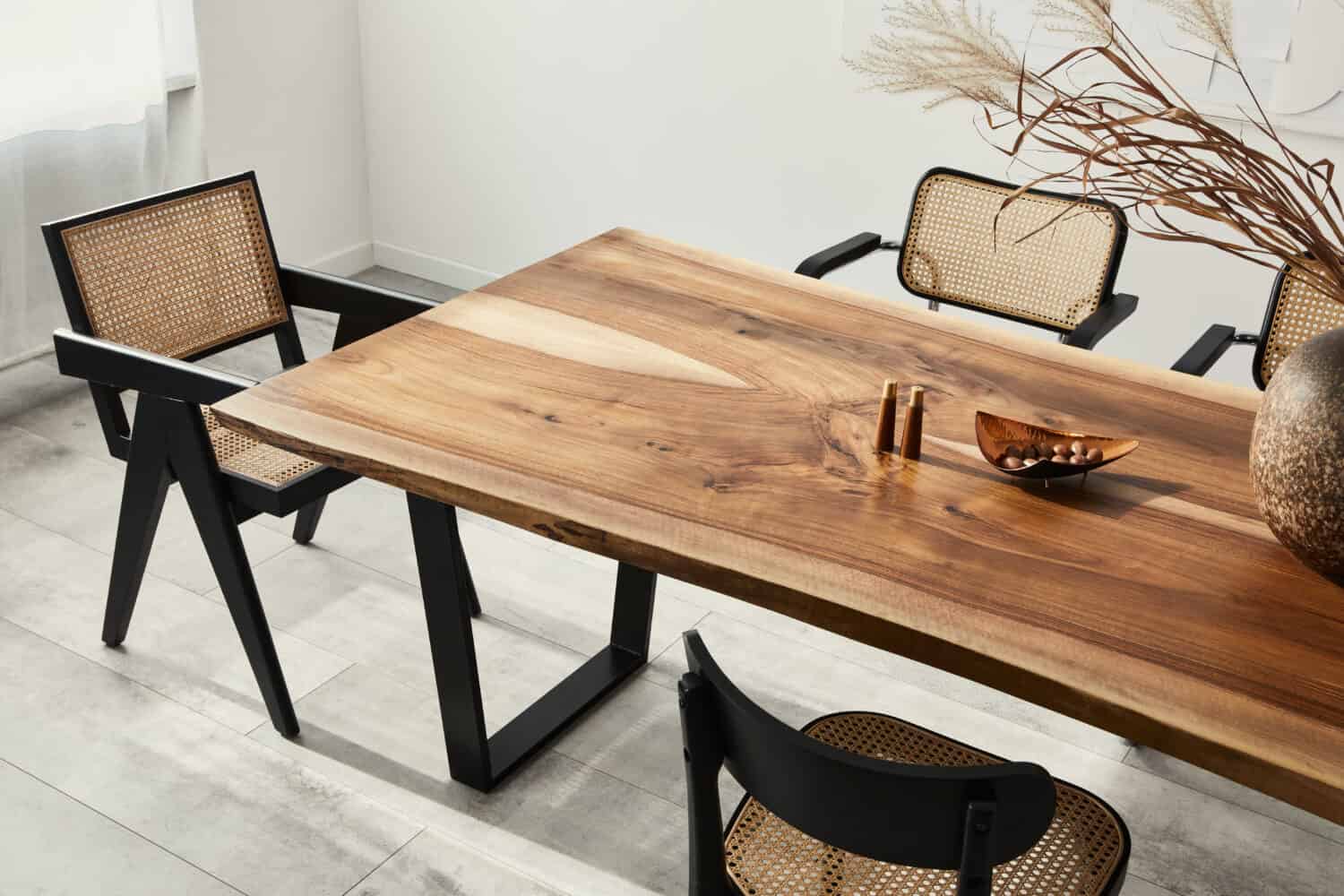 Interior design dell'elegante sala da pranzo con tavolo in legno di famiglia, sedie moderne, piatto con noci, saliera e pepiera.  Pavimento di cemento.  Muro bianco.  Modello.