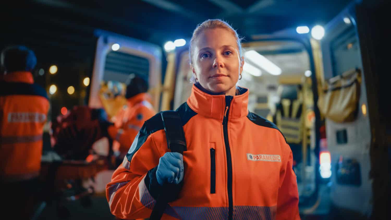 Ritratto di un paramedico femminile EMS in piedi con orgoglio davanti alla telecamera in uniforme medica arancione ad alta visibilità con 