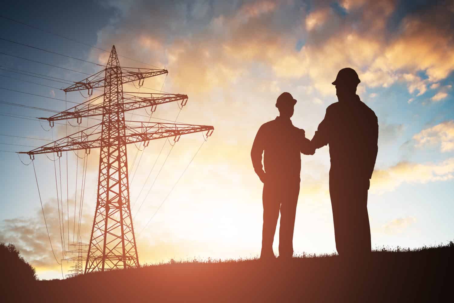 Sagoma di due ingegneri che stringono la mano con il pilone di elettricità contro il cielo drammatico